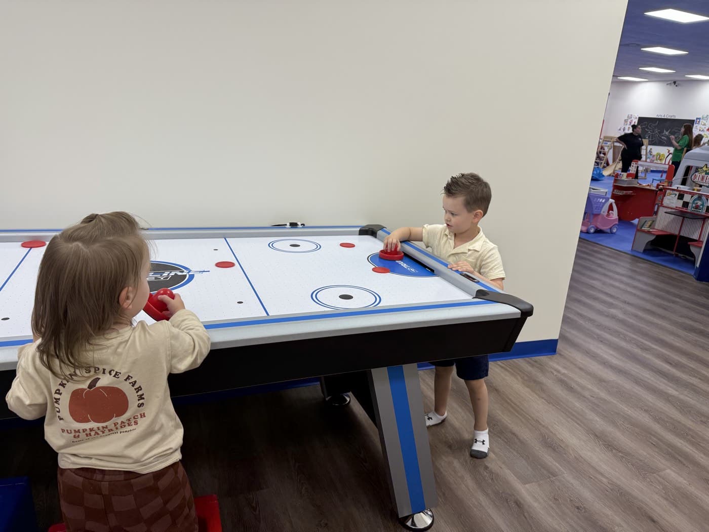 Deux jeunes enfants jouent au hockey de table dans un espace lumineux.
