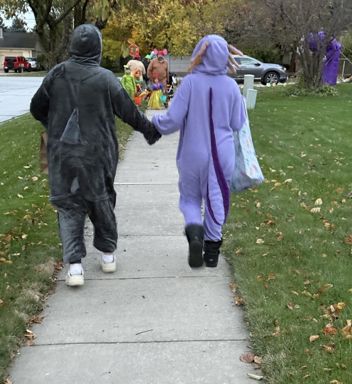 Two girls in costumes walking hand in hand down a sidewalk while trick-or-treating.